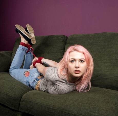 Clothed girl with dyed hair is hog tied with red rope on a chesterfield 40943570