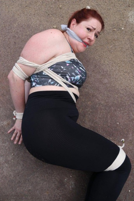 Redheaded girl Mada Rose is left on a paved lot while tied up 82959678