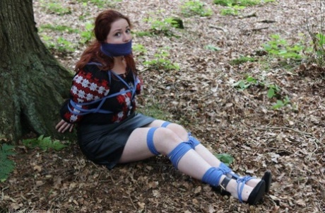 Pale redhead is silenced with a gag while tied up in her clothes under a tree 35774830