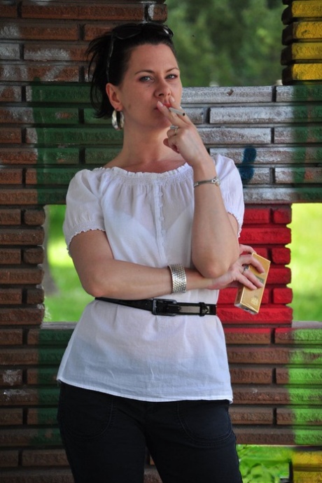 Fully clothed brunette Mina smokes a cigarette in front of a brick wall 23846787