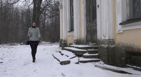 Blonde girl pulls down her leggings to pee on the snow next to a dwelling 82032473